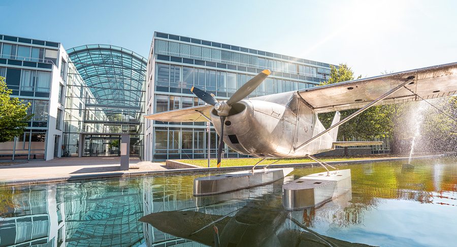 Bürogebäude Skygate in Hallbergmoos mit Glasfassade und Wasserflugzeug-Brunnen im Vordergrund.